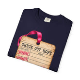 A navy blue folded t-shirt with a graphic print of a vintage check-out tag with a pink ribbon handle and red stamped text, shown on a white background.