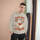 A man wearing a light beige crewneck sweatshirt with a cartoon graphic of a ghost reading a book, surrounded by Halloween elements, with the text &