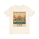 An off-white crewneck t-shirt featuring a vintage-style graphic print of the Library of Alexandria with a classical temple, sailboats, and a sunset.