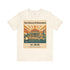 An off-white crewneck t-shirt featuring a vintage-style graphic print of the Library of Alexandria with a classical temple, sailboats, and a sunset.
