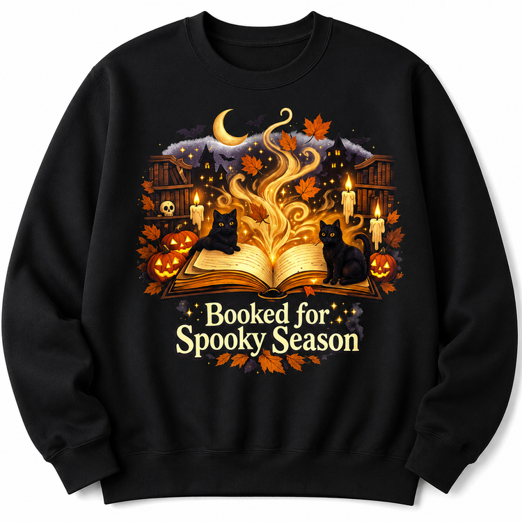 A black crewneck sweatshirt featuring a detailed Halloween graphic on the front. The graphic shows an open glowing book with magical smoke, two black cats, pumpkins, autumn leaves, candles, and a crescent moon, with the text &