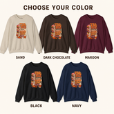 A color selection graphic showing five crewneck sweatshirts labeled SAND, DARK CHOCOLATE, MAROON, BLACK, and NAVY, each with a stack-of-books graphic on the chest under the heading &