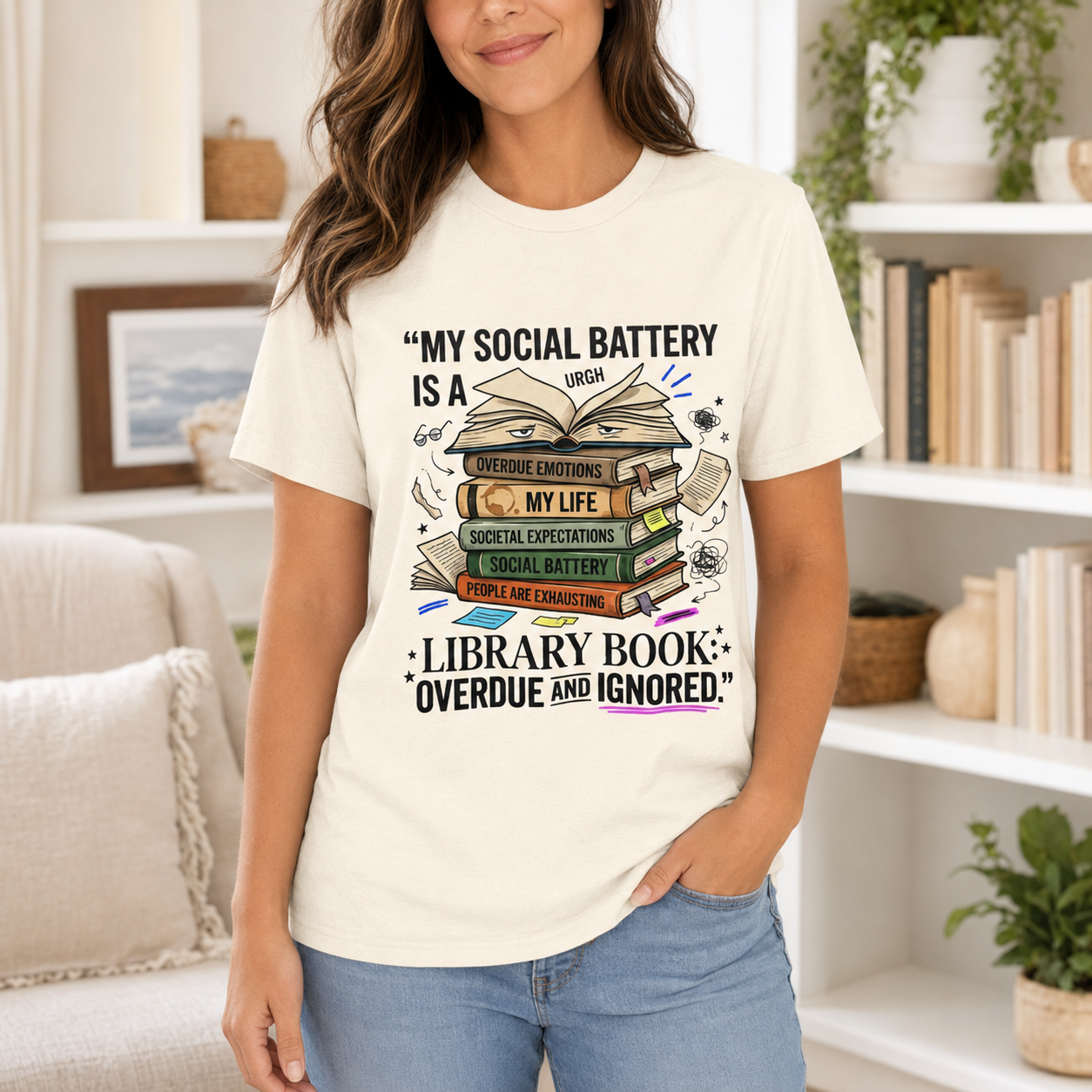 A woman wearing a cream-colored graphic t-shirt with a book-themed print and text, paired with light blue jeans, standing in a cozy, brightly lit living room.