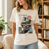 A woman wearing a cream-colored graphic t-shirt with a book-themed print that reads &