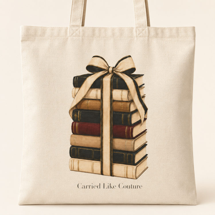 A natural canvas tote bag featuring a graphic of a stack of vintage books tied with a cream ribbon, with the text &
