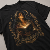 A black short-sleeve t-shirt featuring a detailed graphic print of a woman holding an open glowing book, surrounded by a crescent moon, stars, laurel wreath, and snakes, with the text &
