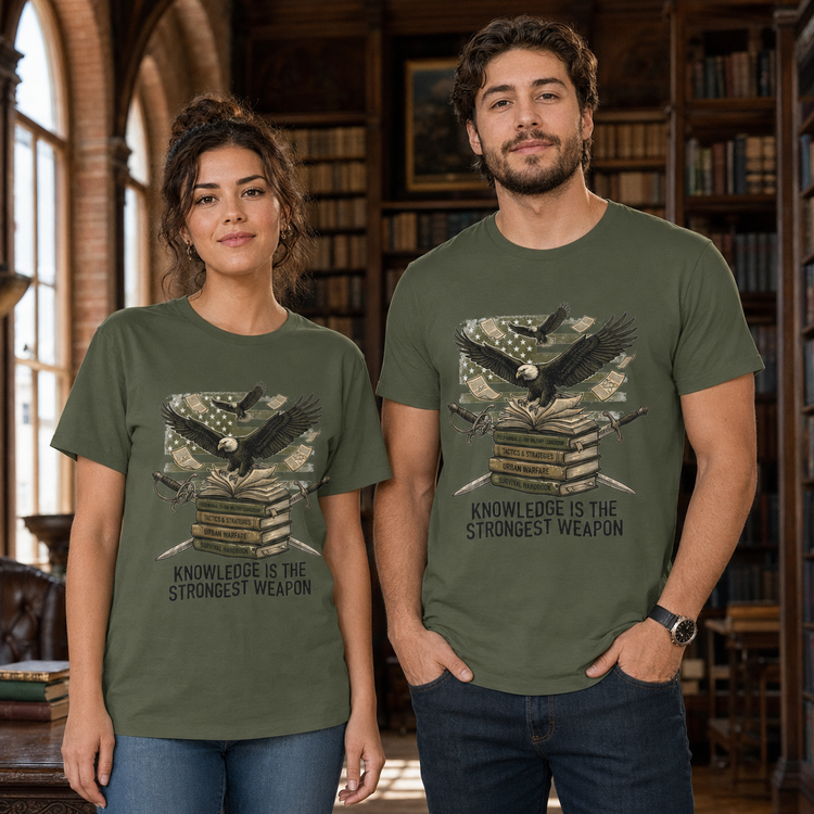 A man and a woman wearing matching olive green graphic t-shirts in a library setting. The shirts feature a graphic of a raven perched on a stack of books with a skull and American flag, and the text &