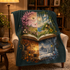 A dark teal throw blanket draped over a cream armchair in a cozy living room. The blanket features a large, colorful printed design of an open book with four quadrants showing different seasons: pink cherry blossoms, a sunny coastal landscape, autumn foliage, and a snowy winter night scene.