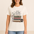 A woman wearing a cream-colored graphic t-shirt with a book-themed print that reads &