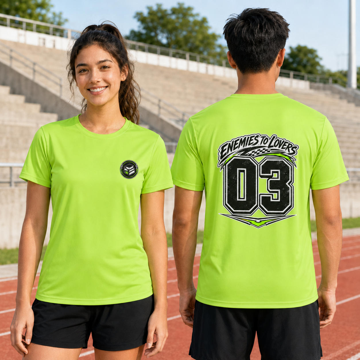A man and a woman modeling a bright lime green athletic t-shirt on an outdoor track and field stadium. The woman shows the front of the shirt with a small black circular logo on the left chest, and the man shows the back with a large graphic reading &