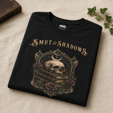A folded black t-shirt with a gothic-style graphic print featuring a skull on stacked books, roses, and the text &