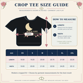 A crop tee size guide infographic showing a black graphic t-shirt with a crescent moon and floral print, measurement arrows, a sizing table from XS to 2XL, and instructions on how to measure garment length and width.