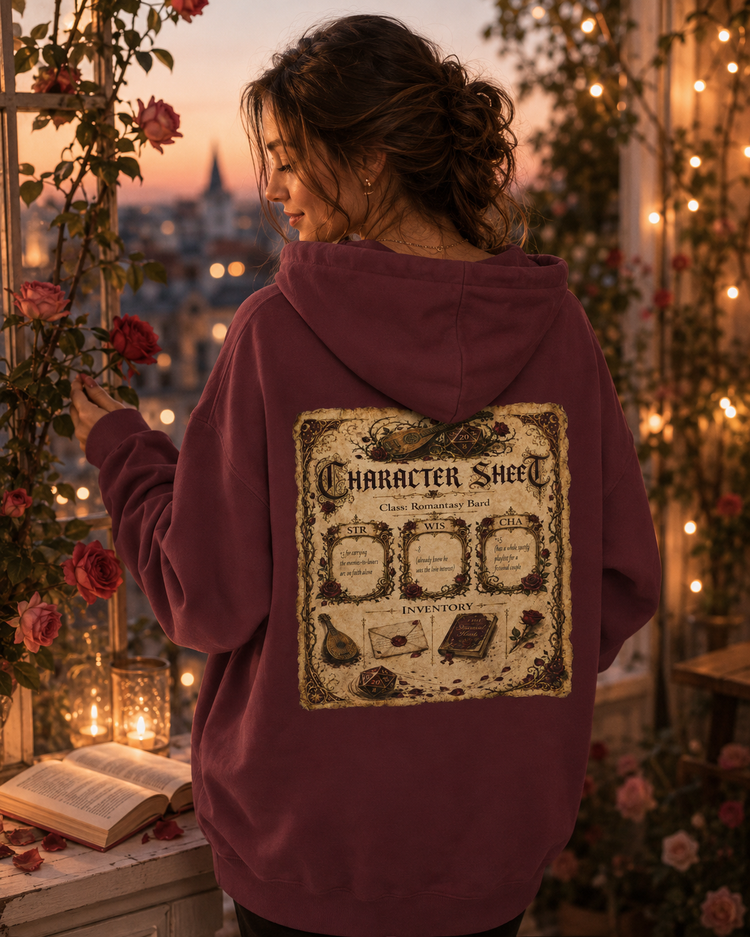 A woman stands on a balcony at dusk wearing a burgundy hoodie with a large vintage-style character sheet graphic printed on the back. The scene is decorated with roses, string lights, candles, and an open book in the foreground.