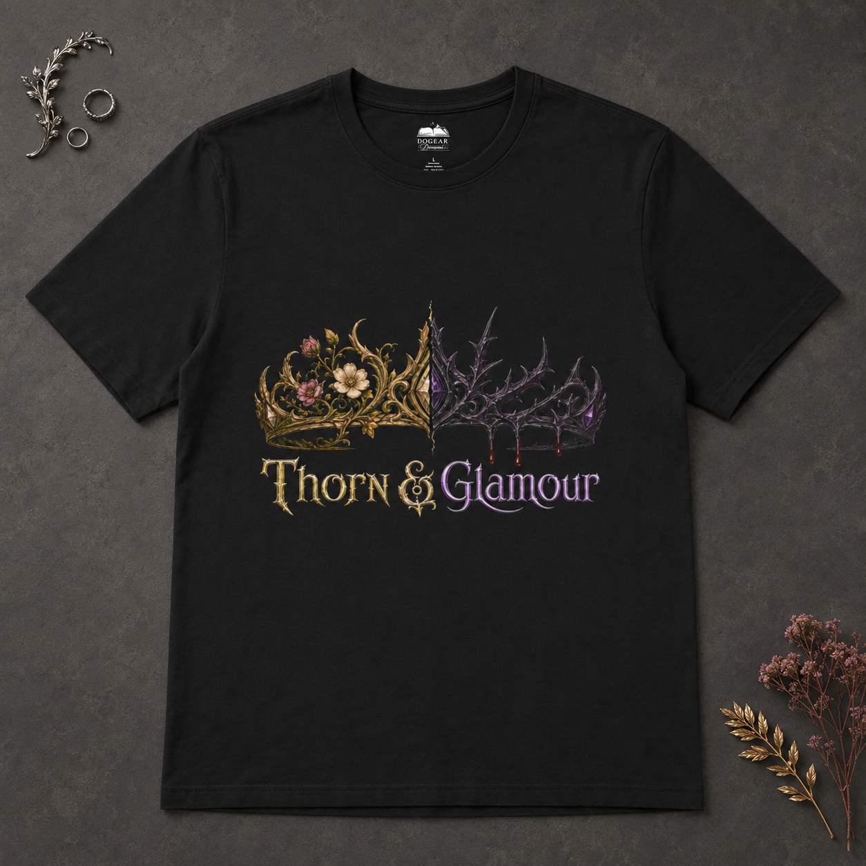 A black short-sleeve graphic t-shirt laid flat on a dark textured background, featuring a split design with a gold floral crown on the left and a purple thorny crown on the right, with the text &