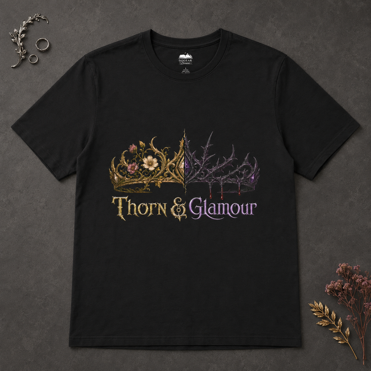 A black short-sleeve graphic t-shirt laid flat on a dark textured background, featuring a split design with a gold floral crown on the left and a purple thorny crown on the right, with the text &