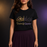 A woman wearing a black short-sleeve graphic T-shirt with a gold and purple gothic crown design and the text &