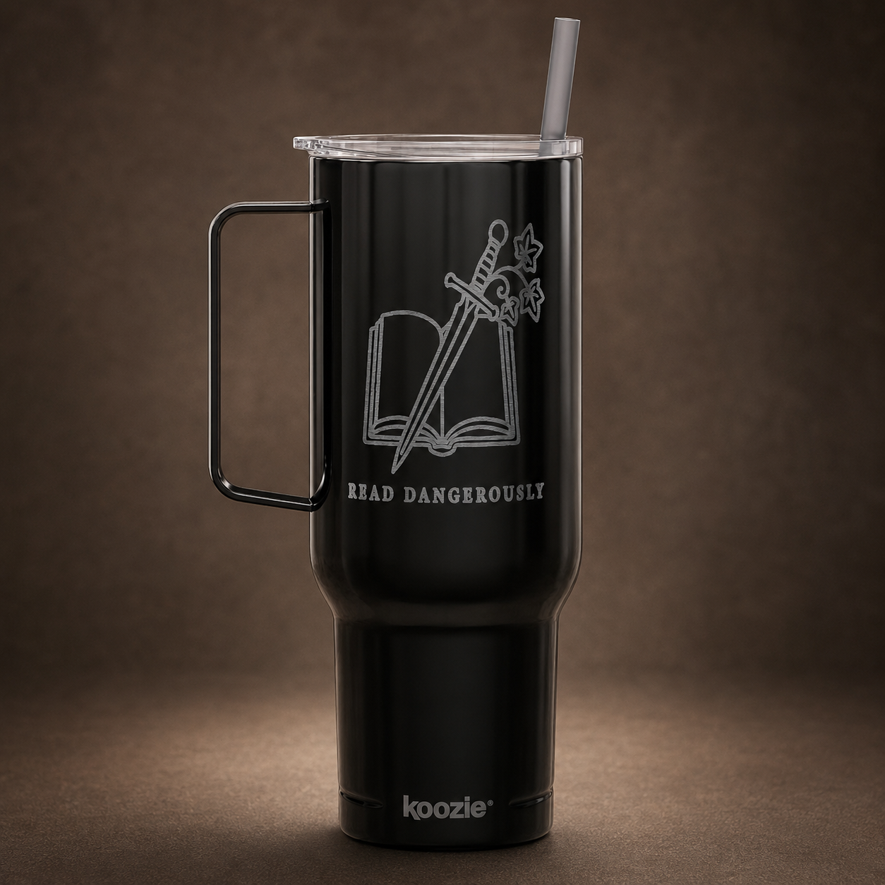 A black insulated travel tumbler with a handle and clear lid, featuring a white laser-engraved design of an open book with a sword and the words &