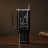 A matte black insulated tumbler with a handle, clear lid, and straw, featuring a white laser-engraved design of an open book and sword with the text &