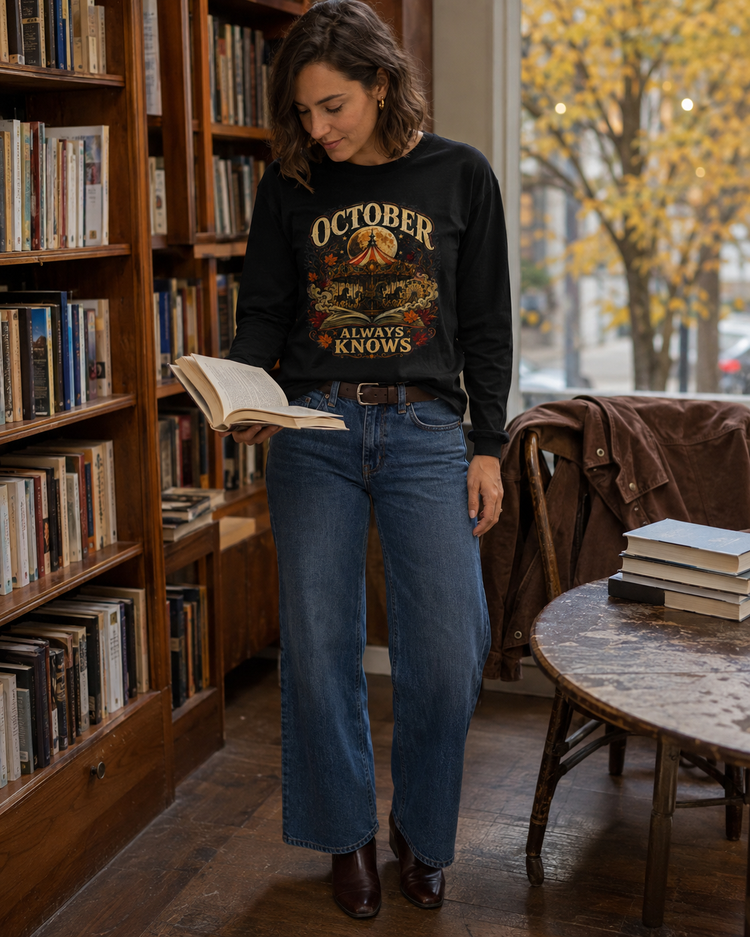 A woman stands in a cozy bookshop reading, wearing a black crewneck long-sleeved tee with a vintage-style graphic that reads &