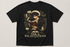 A black short-sleeve graphic t-shirt featuring an illustration of a young man reading a book surrounded by magical items, with the text &