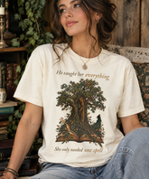 A woman wearing a cream-colored graphic t-shirt with a tree and book illustration, sitting in a cozy, rustic room setting.