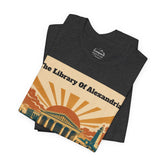 A folded dark heather gray t-shirt with a vintage-style graphic print of the Alexandria Library. The graphic features a beige background with a retro sunburst in orange and yellow, and a teal-colored library building.
