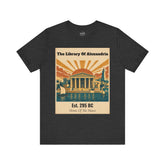 A dark heather gray t-shirt with a vintage-style graphic print on the front. The graphic features a beige background with retro illustrations of the Library of Alexandria, including columns, a sunburst, sailboats, and a lighthouse, with text reading &