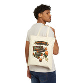A man wearing a white t-shirt and blue jeans is shown from the back, carrying a cream canvas tote bag over his shoulder. The tote bag features a colorful graphic print with the text &