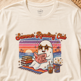An off-white crewneck t-shirt featuring a colorful retro graphic of a ghost reading a book on a beach with the text &
