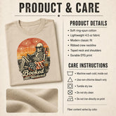 A folded beige graphic T-shirt shown on a textured cream background with printed product details, care instructions, and a fabric close-up. The shirt features a large retro skeleton lounge graphic with fireworks, an American flag, a drink, and the text &